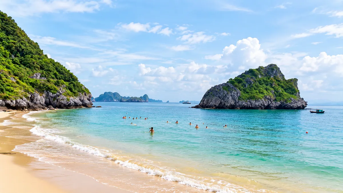 Cat Ba sandy beach with swimmers and limestone islands